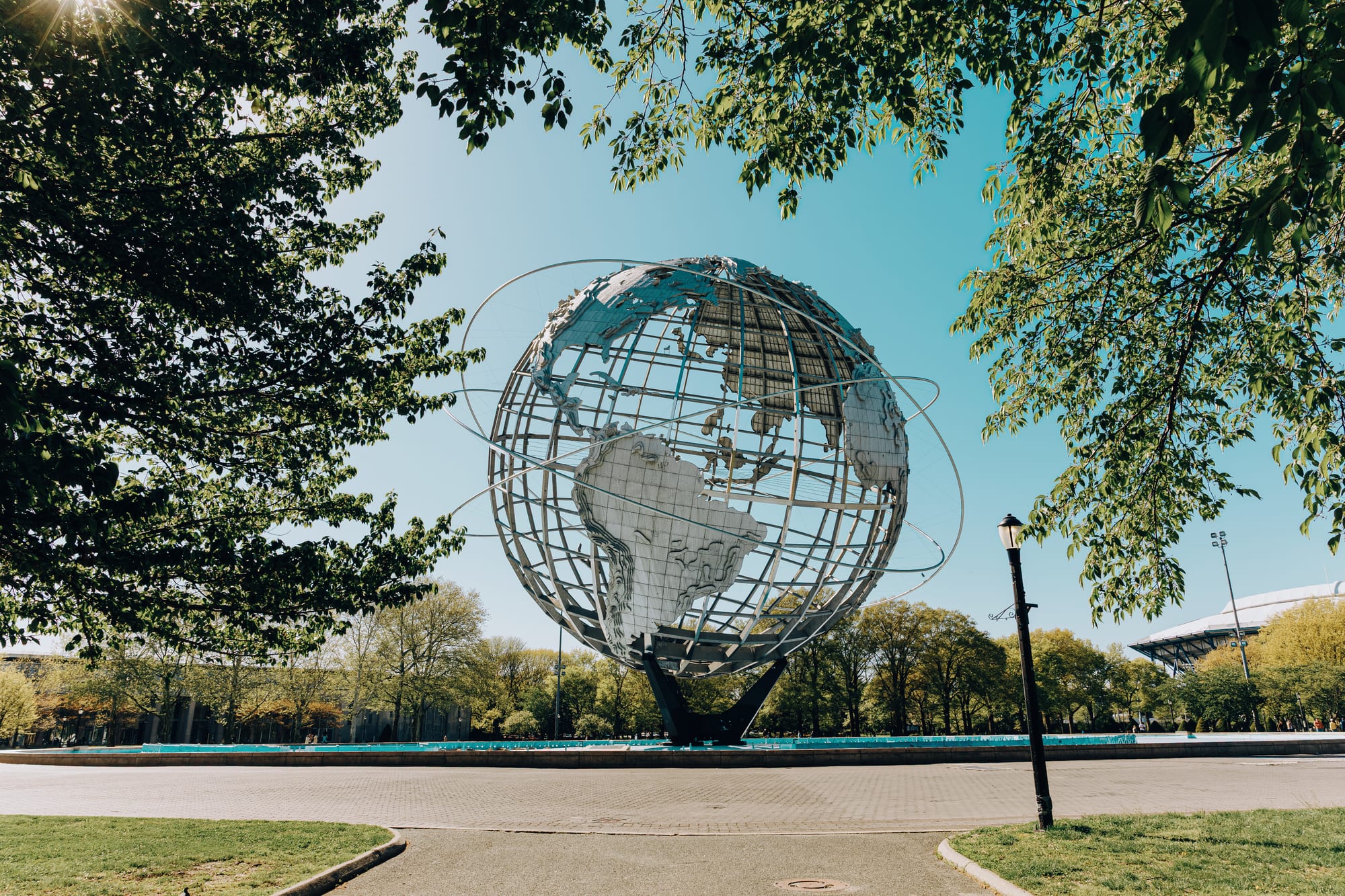 The Unisphere at Flushing Meadows-Corona Park framed by spring foliage, with the USTA National Tennis Center visible in the background